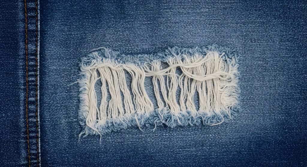 Closeup of distressed denim fabric with ripped hole and frayed edges detailed texture of blue jeans